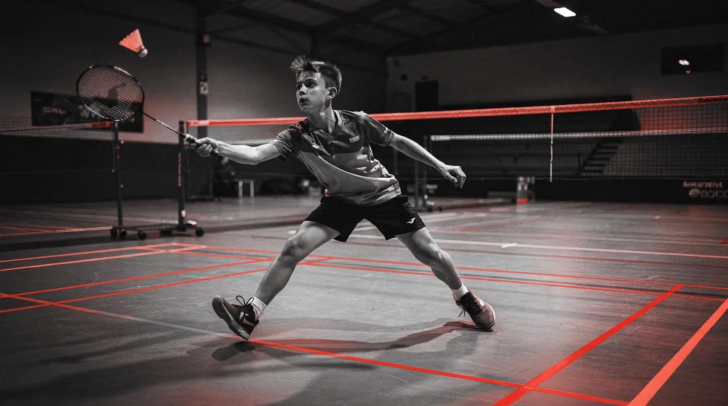 young badminton player mid-smash on an academy court, the sports for life whatsapp ai agent case study